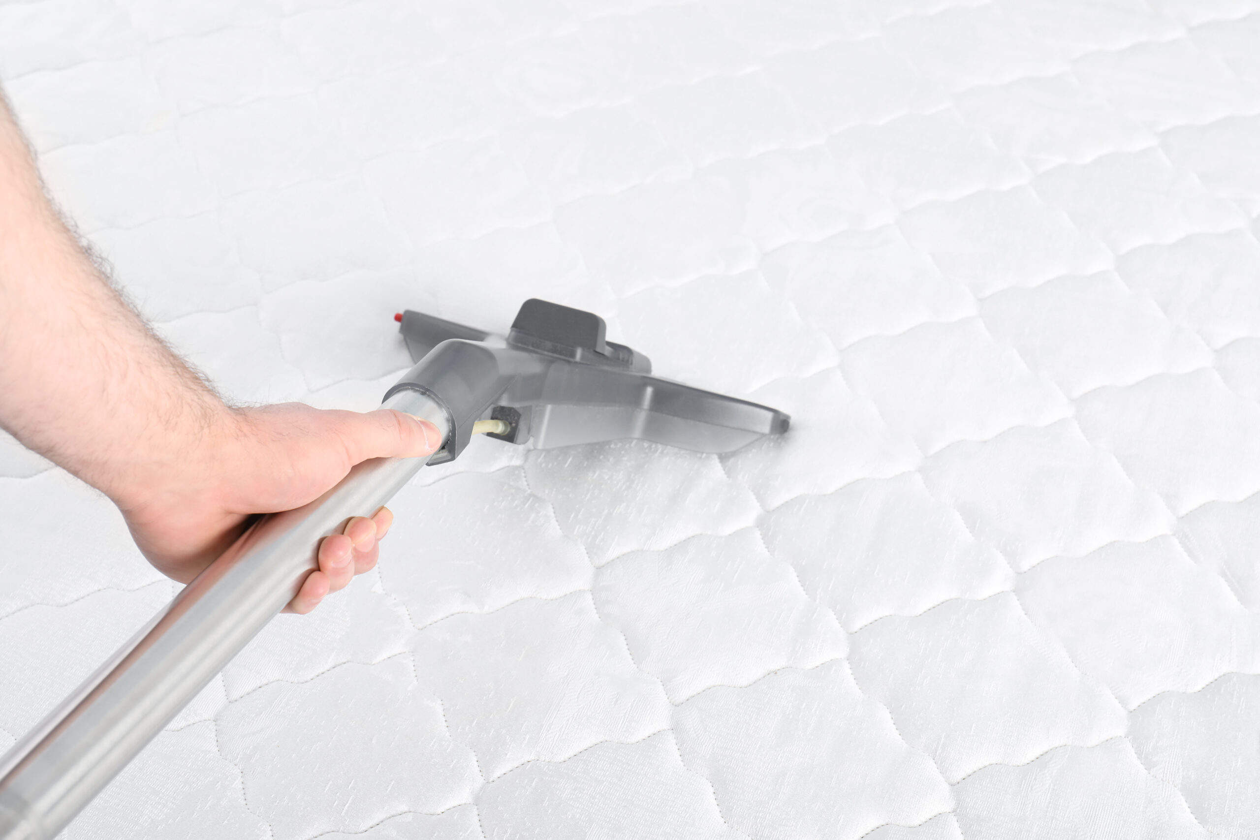 Man disinfecting mattress with vacuum cleaner